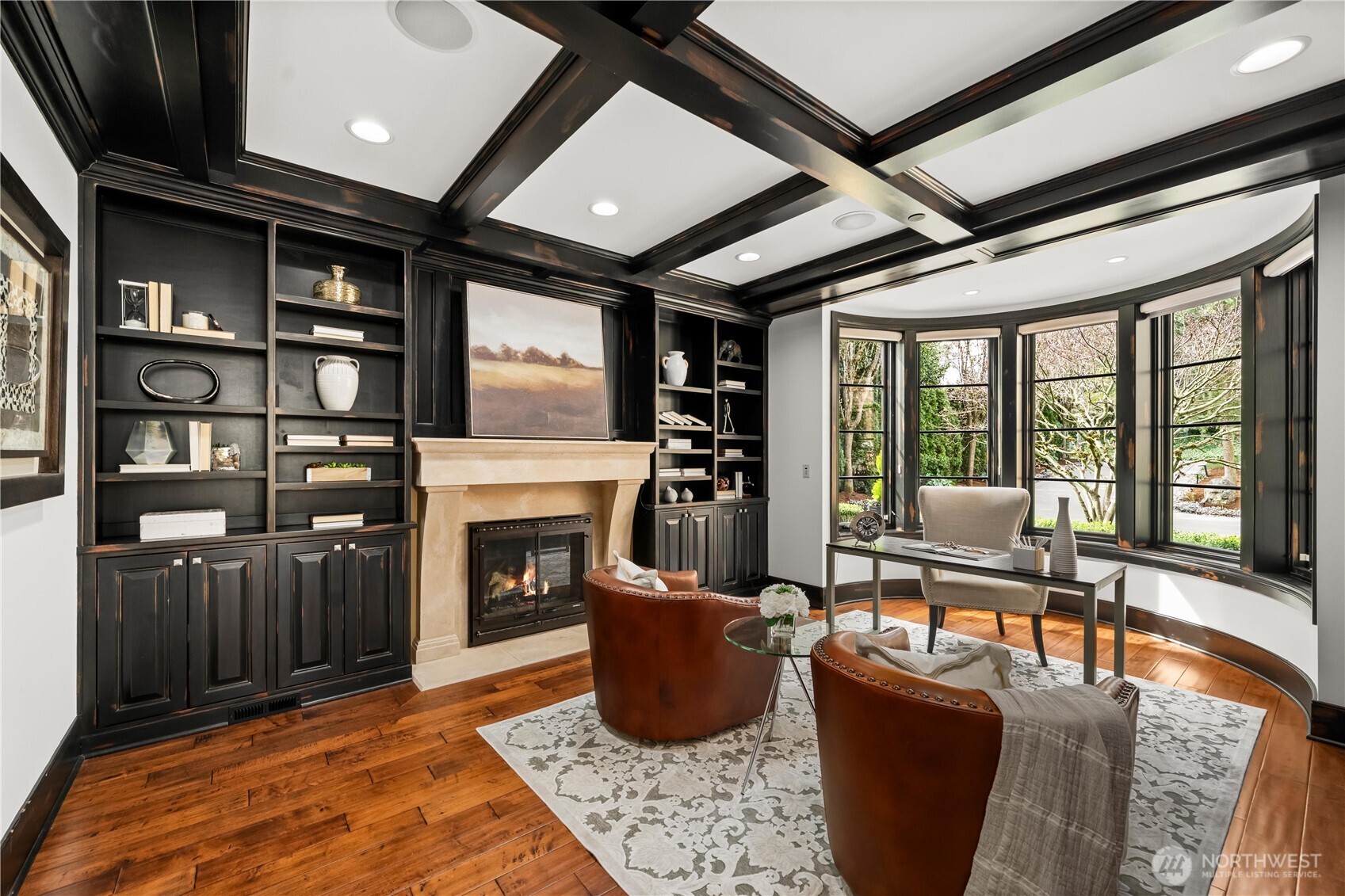 Refined office with custom built-ins, coffered ceiling, and a bay window bringing in natural light.