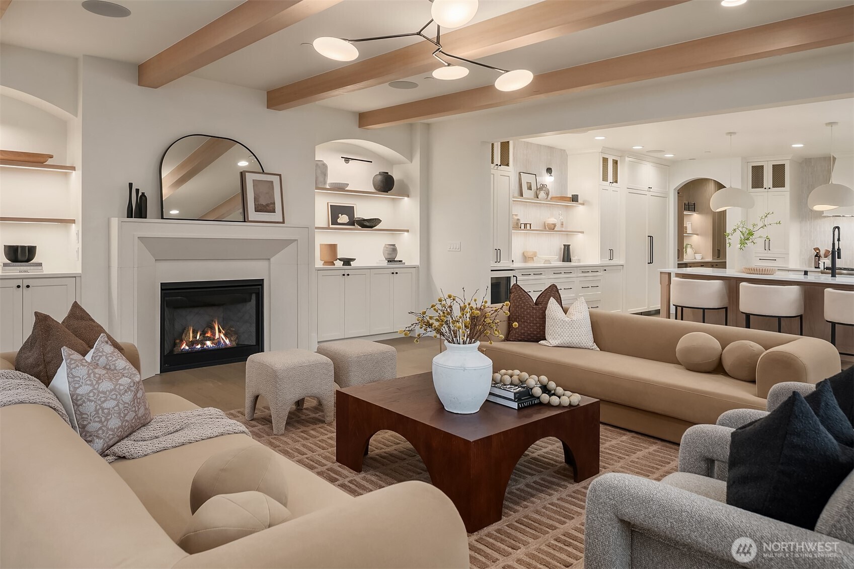 Inviting great room featuring exposed wood beams, a statement fireplace, and arched built-in shelving, creating a warm yet elevated space for gathering.