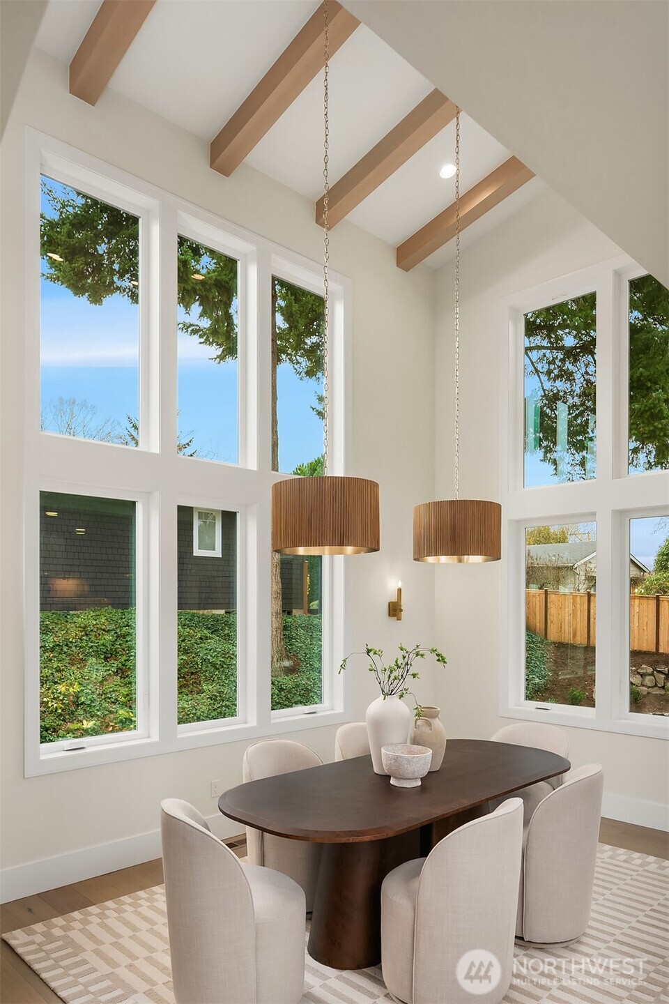 Light-filled dining area featuring over 18-foot ceilings, exposed wood beams, and expansive windows that create an airy, elevated gathering space.