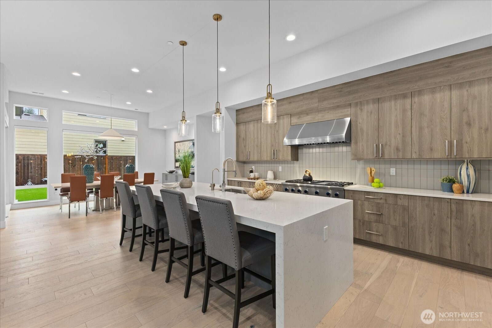 A beautifully composed culinary space where the oversized island, warm wood tones, and effortless flow to the dining area create a kitchen that is as inviting as it is sophisticated.