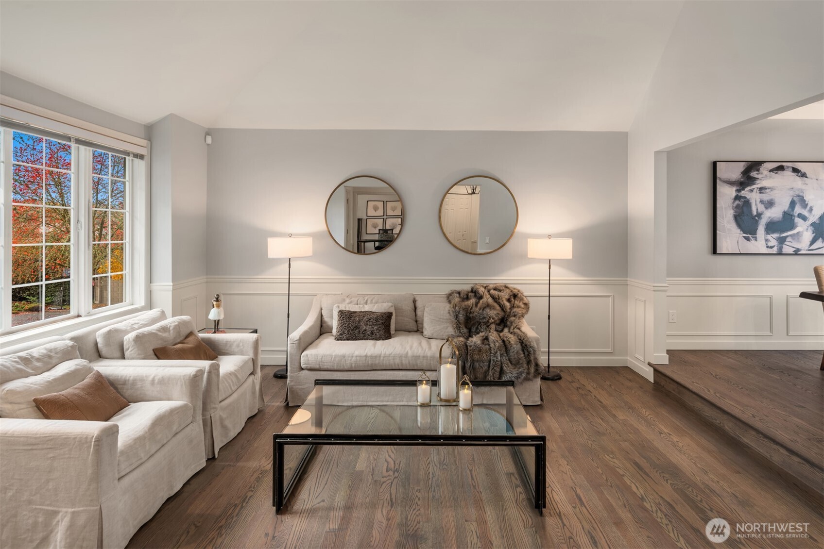 Sunny, south-facing sunken living room features expansive mullioned windows with territorial views, wainscotting, real oak hardwoods, and vaulted ceilings.