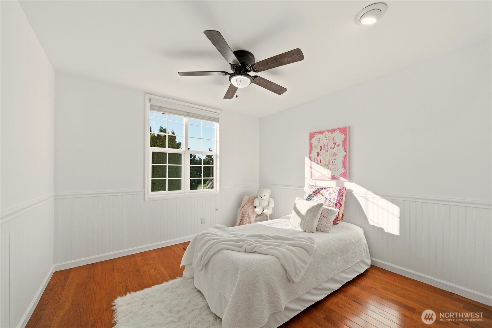 Bright bedroom featuring wainscoting detail and an oversized window.