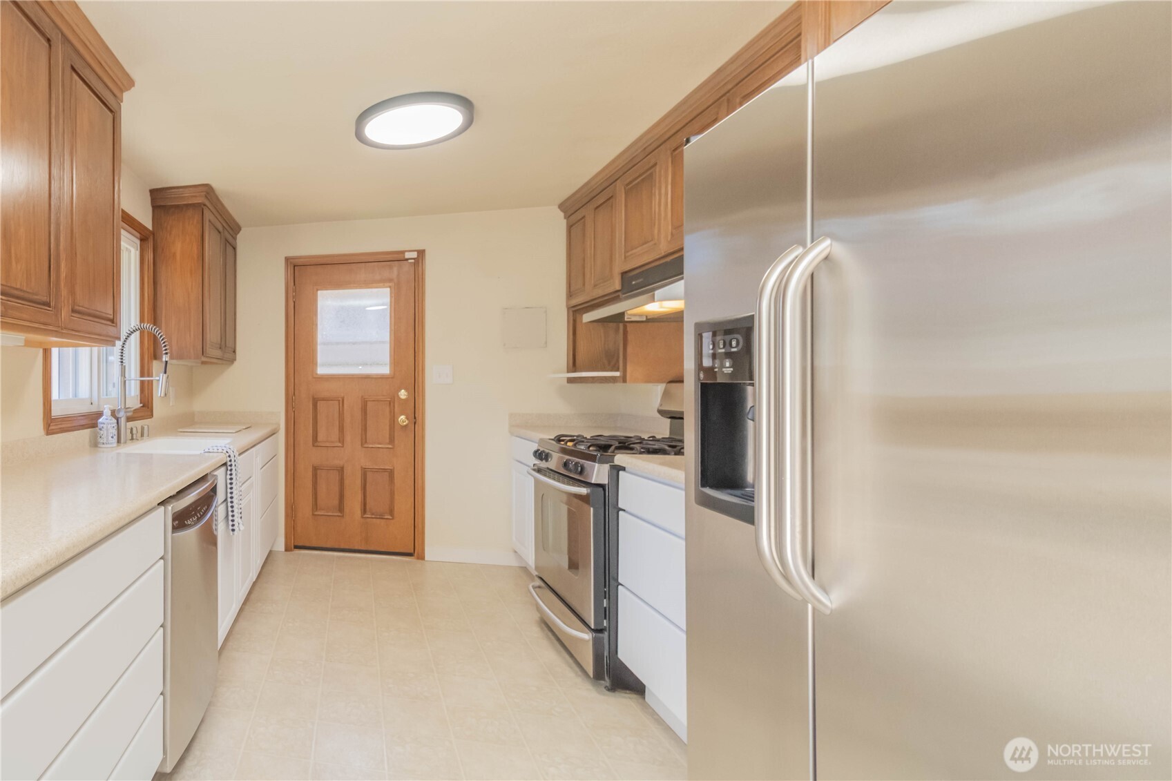 Good size kitchen with two-toned cabinets, stainless appliances, custom Corian counters with bonus cutting board but-outs, with slider to deck
