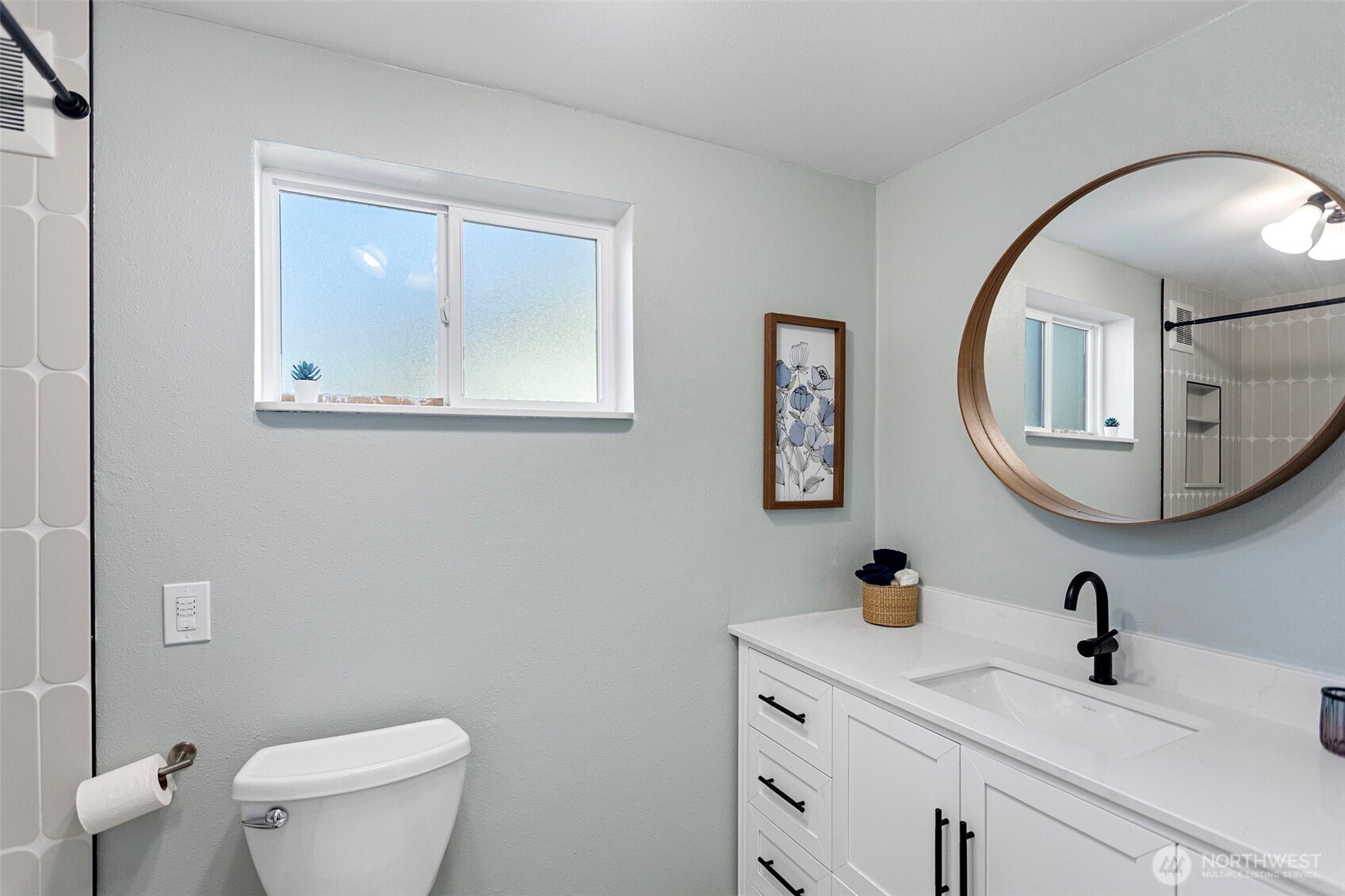 The full bath serves both daylight bedrooms — white shaker vanity, matte black hardware, warm wood-framed mirror, and a custom tile shower surround. Renovated, windowed, and finished with care.