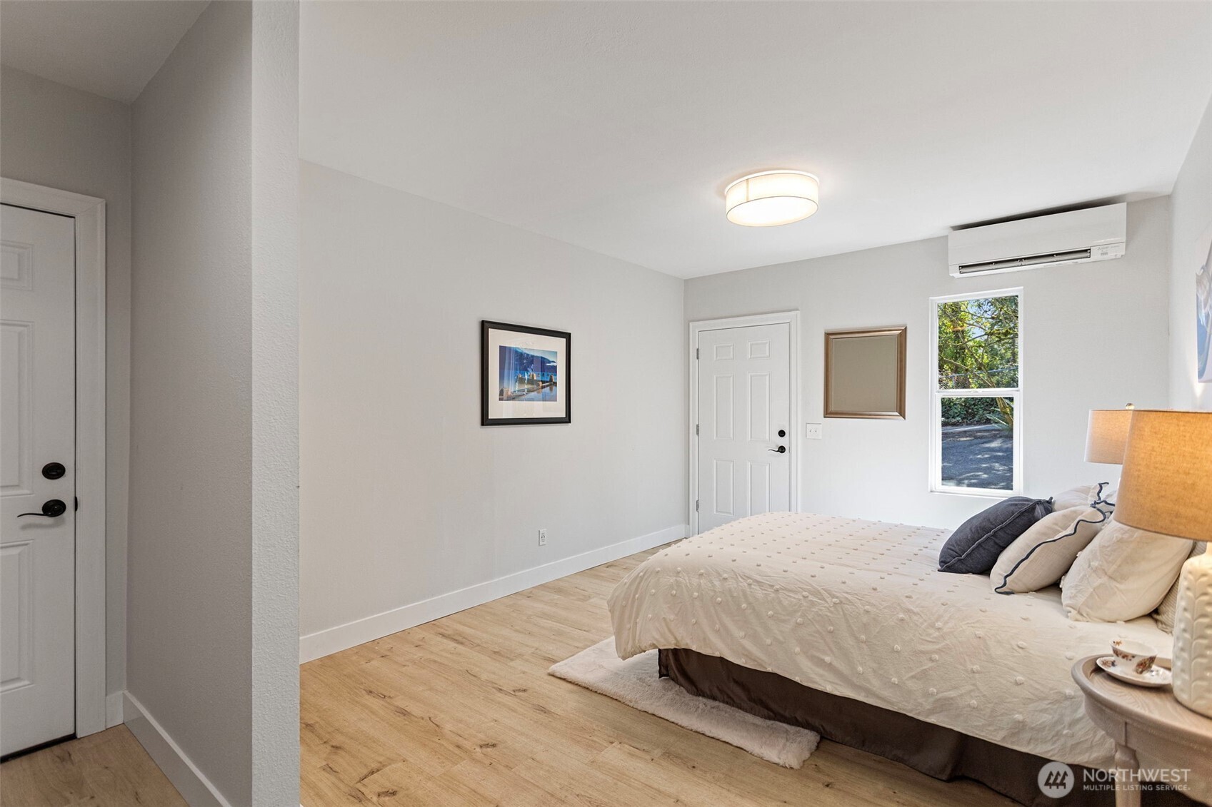 The primary bedroom: mini-split, LVP flooring, and three ways out — driveway, garage, and the exterior storage room.