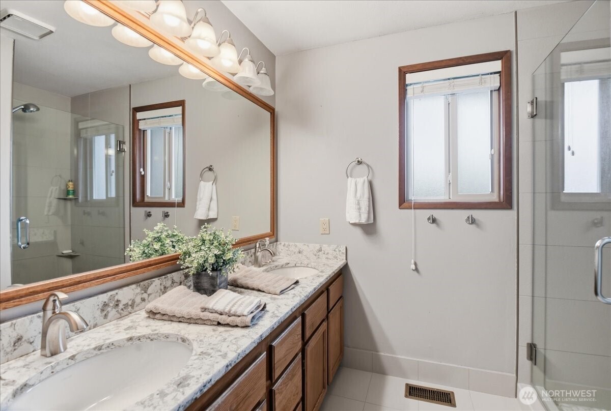 Updated primary bath with dual sinks, quartz counters, tile floors, and a glass-enclosed tile shower.