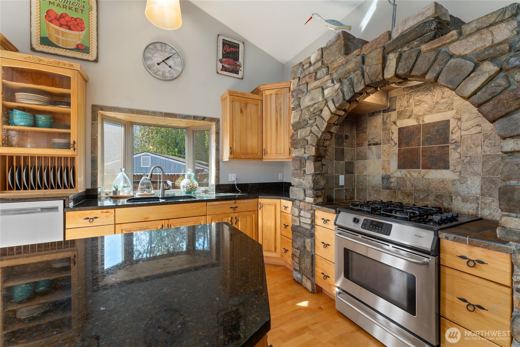 View 3 of kitchen w/ hardwood floors, stainless steel appliances, quartz countertops, wood beams, stone surround stove and oven, double sink and large windows with views of Lake Chelan.