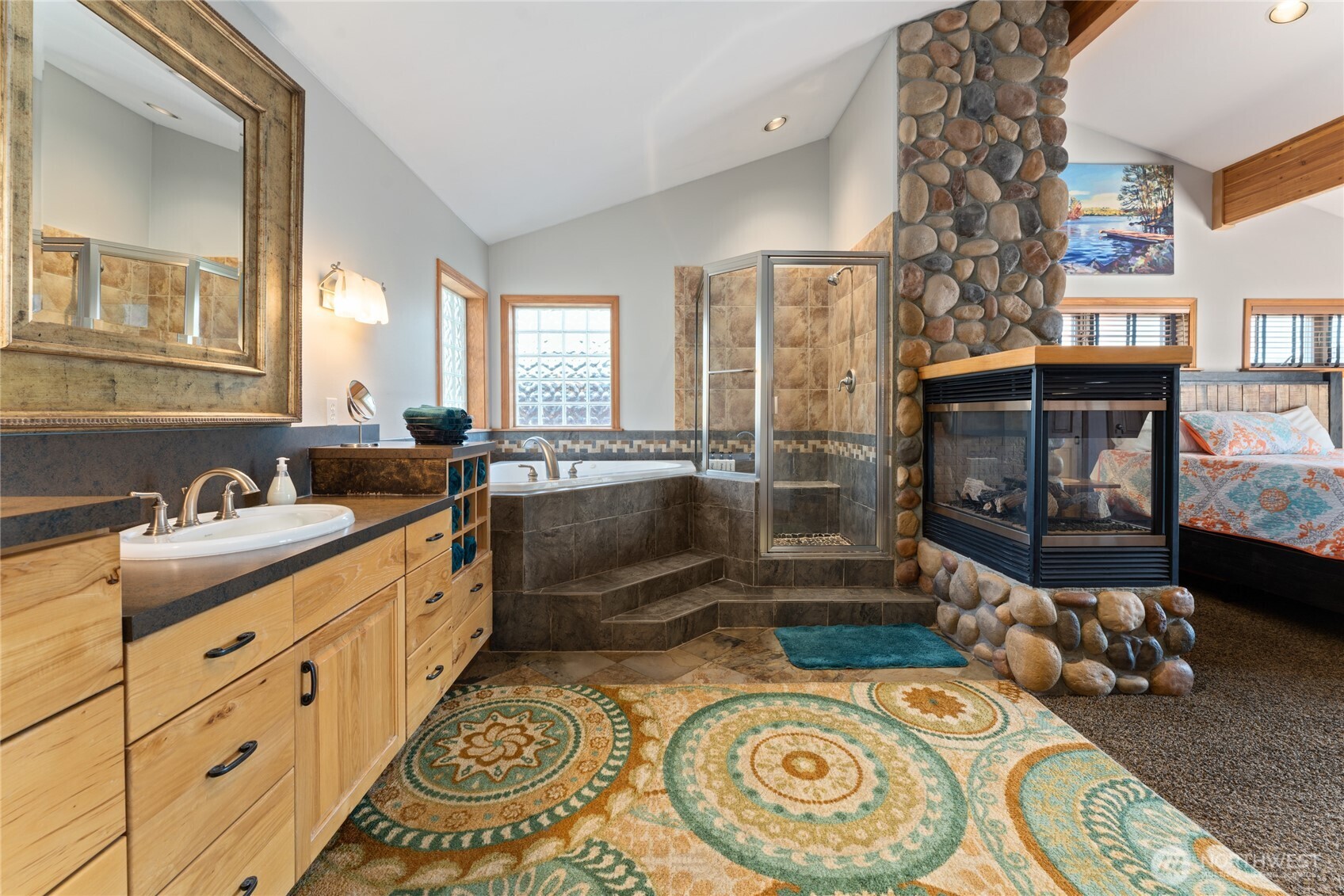 View of main level Primary Bedroom bathroom suite w/ stone fireplace, quartz countertops and soaking tub.