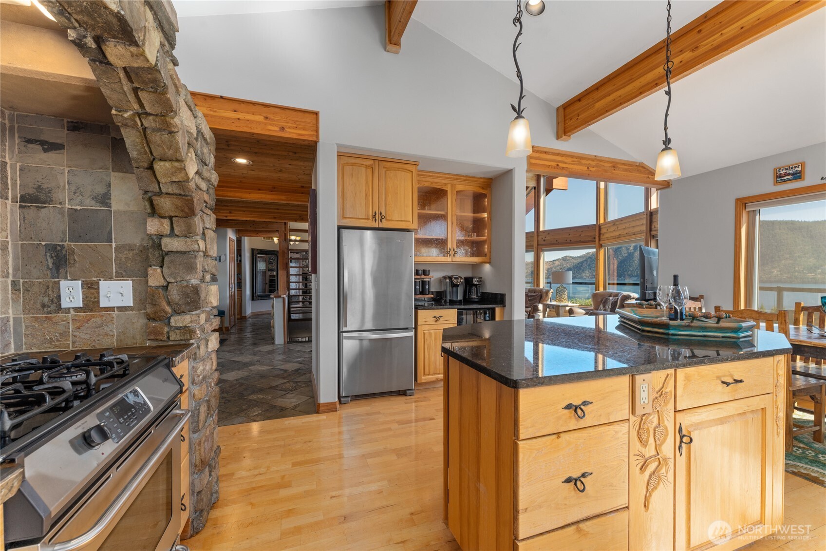 View 1 of kitchen w/ hardwood floors, stainless steel appliances, quartz countertops, wood beams, stone surround stove and oven and large windows with views of Lake Chelan.
