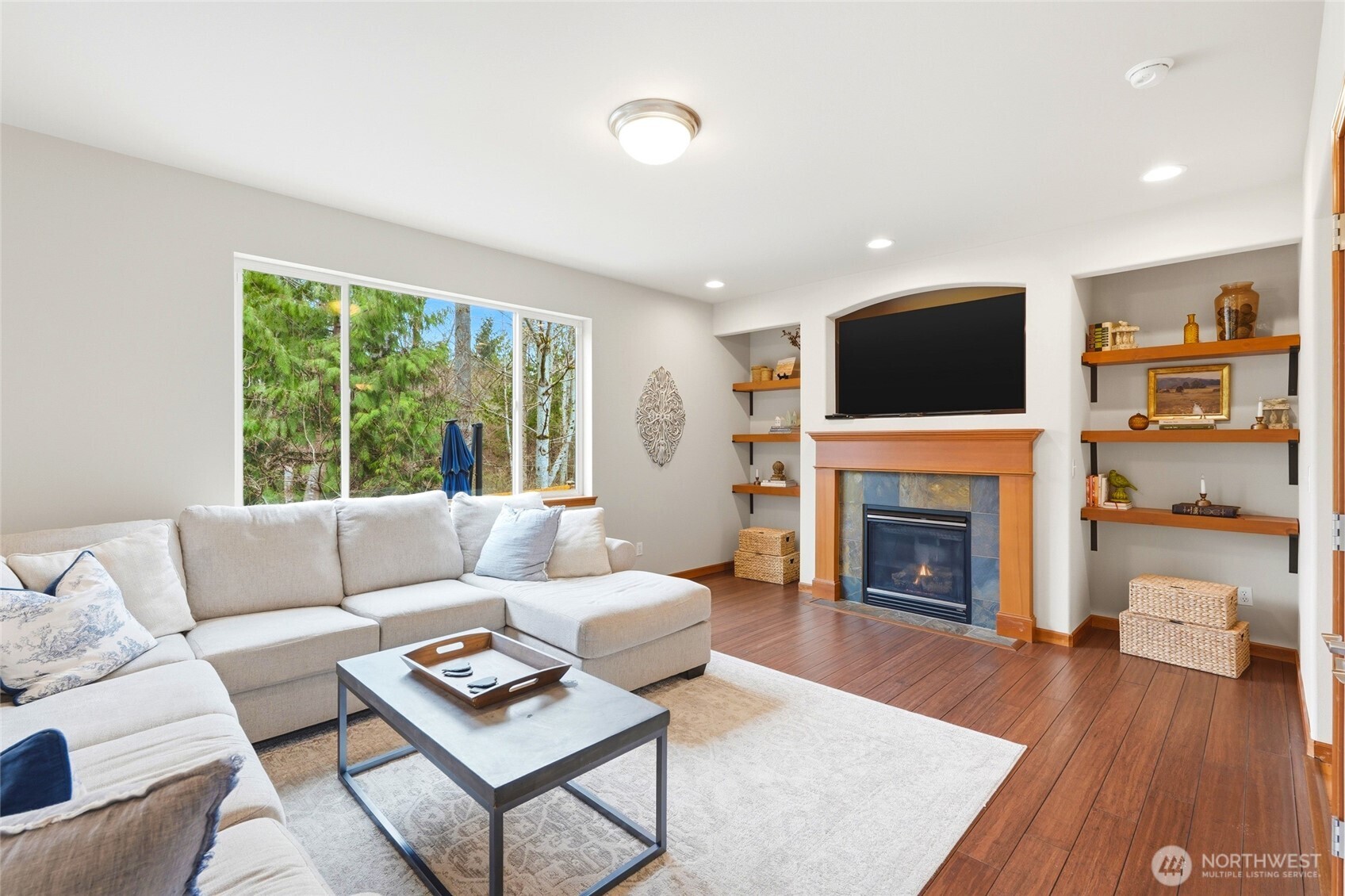 The kitchen opens to a large family room with a gas fireplace and picture windows framing the wooded backdrop.