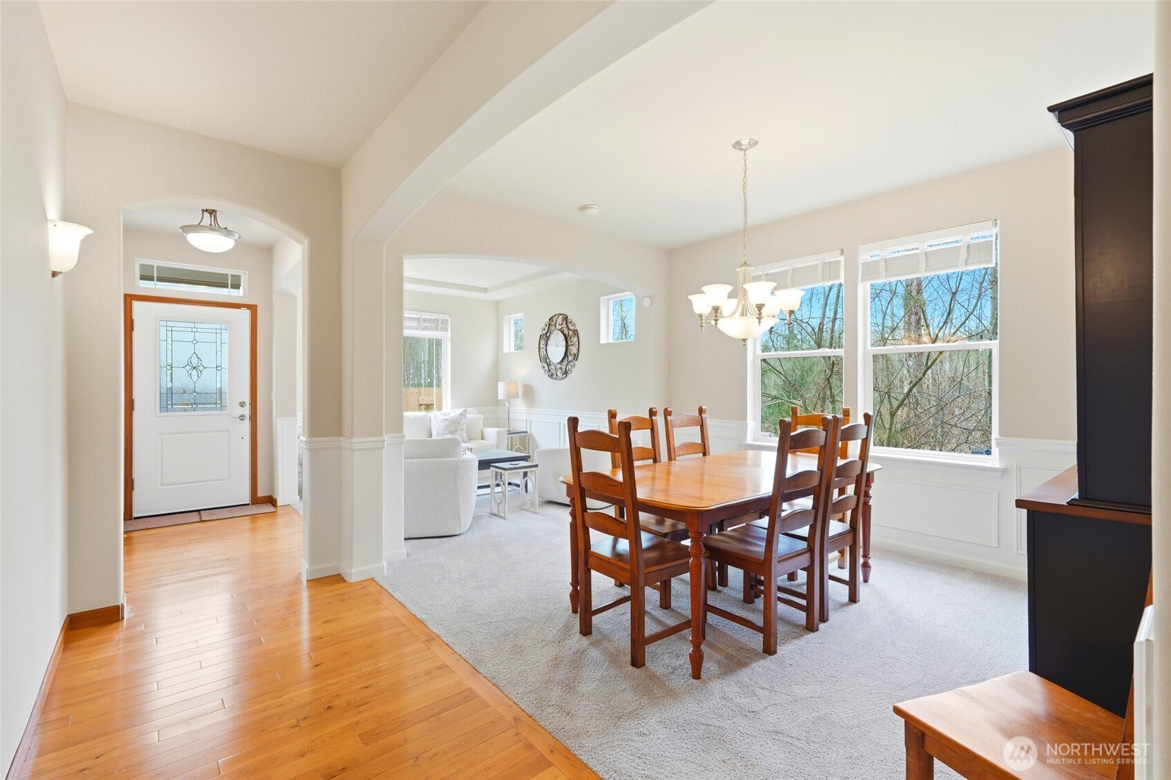 Formal dining room with chandelier, wainscoting, and large windows overlooking trees