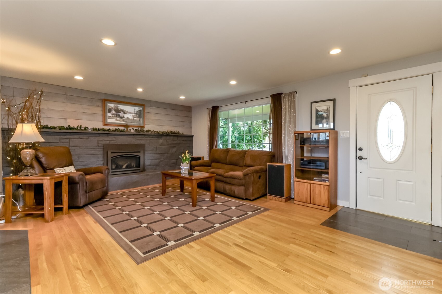 As soon as you step through the door, warmth greets you from the gleaming hardwood floors. The centerpiece is the full wall gas fireplace. A flood of natural light streams in brightening the space and highlighting the rich tone of the wood and stone. The open concept layout seamlessly connects living areas, creating an airy, welcoming flow that makes the home feel instantly inviting.