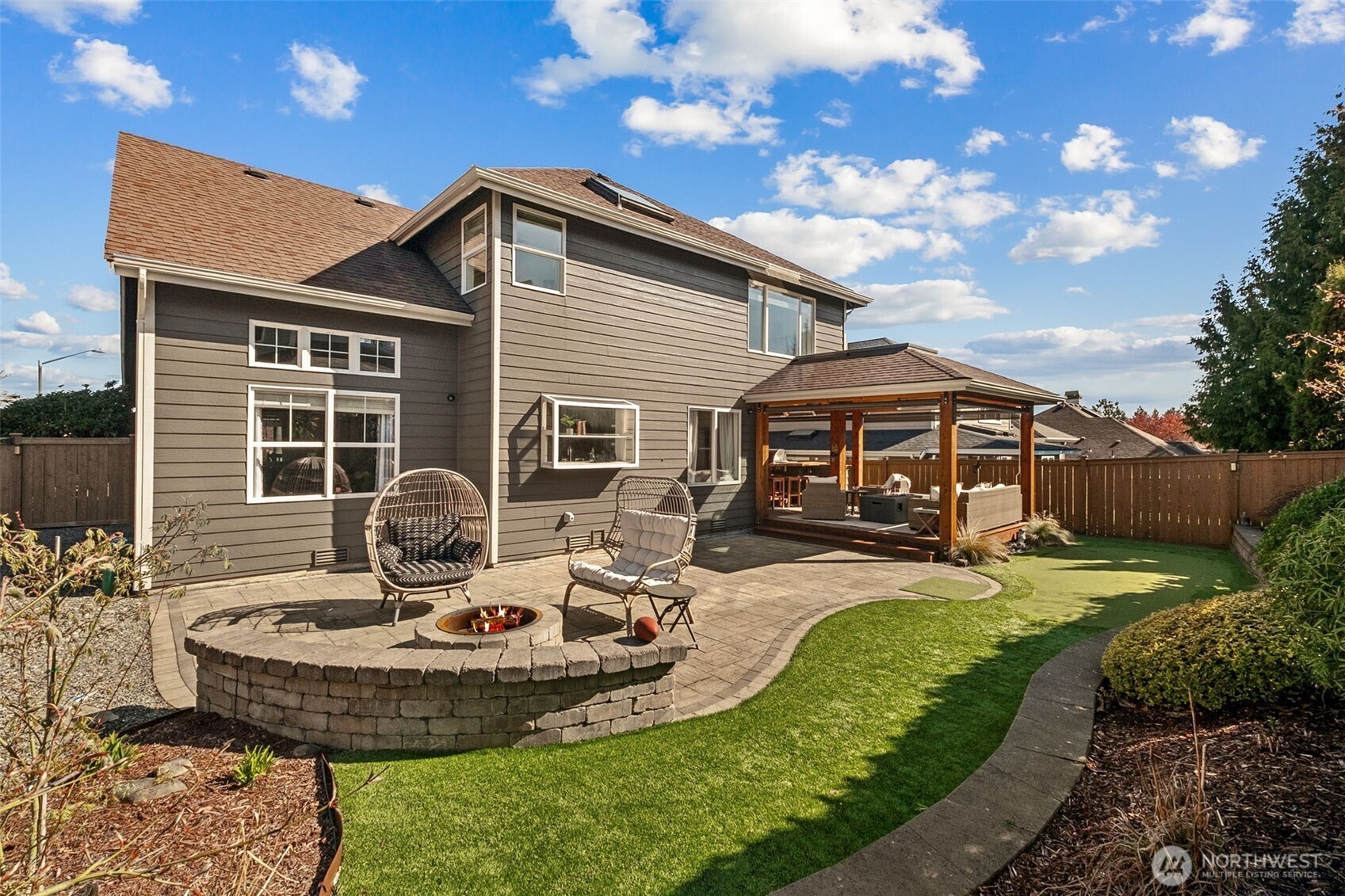 Fully fenced backyard with a large paver patio, built-in fire pit with seating, artificial lawn, the covered outdoor living area AND a putting green—perfect for entertaining and everyday enjoyment!