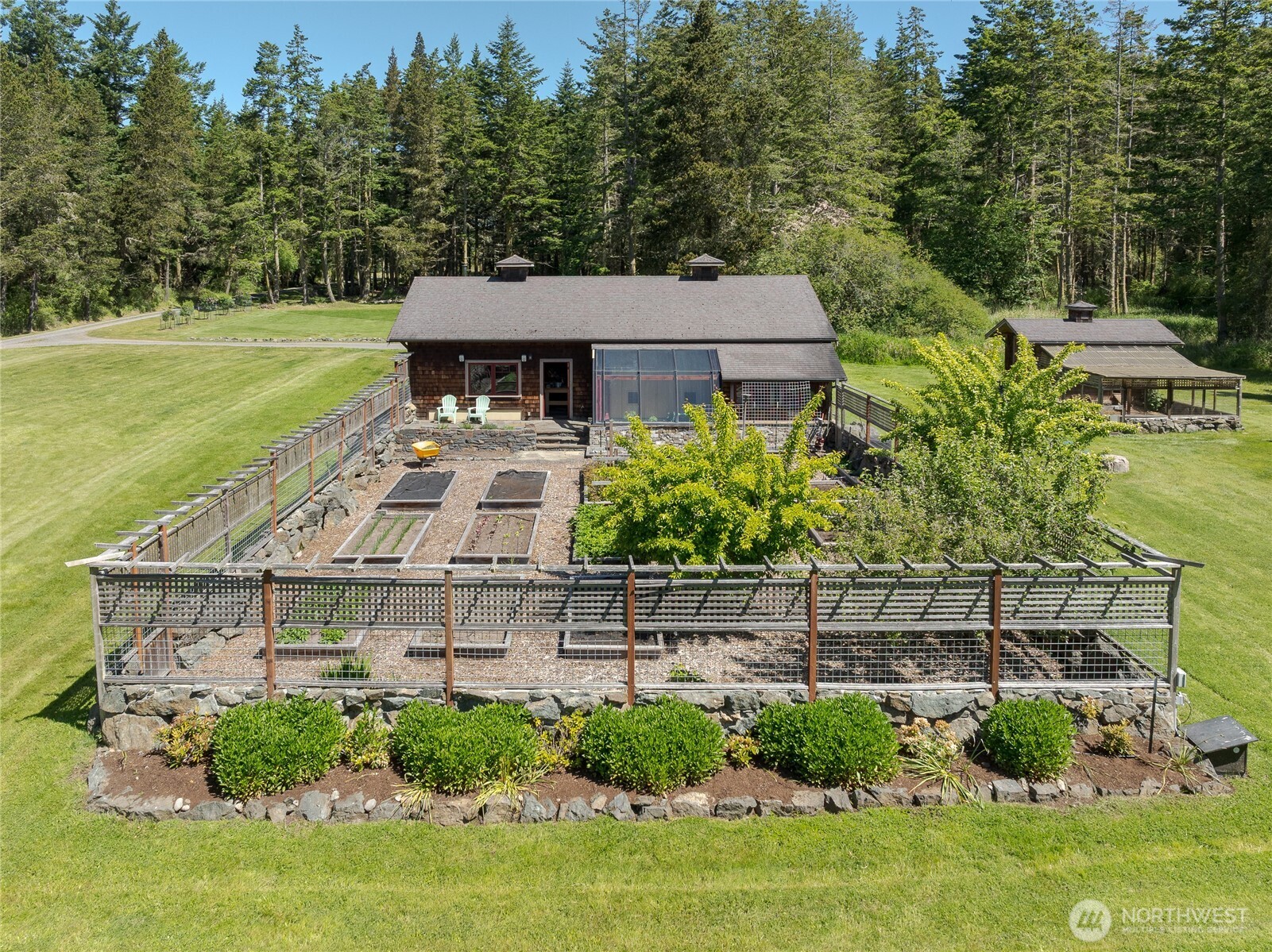 Large shop/garage with attached greenhouse overlooks the fenced garden with fruit trees.  Elegant chicken house to the right.