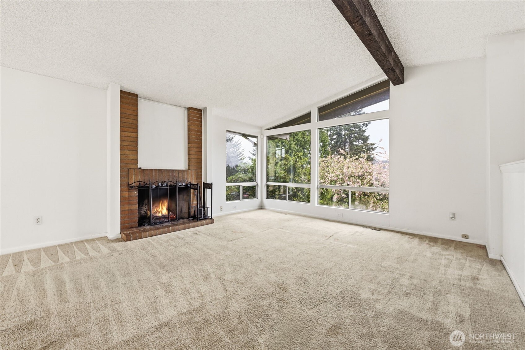 Generous living room with vaulted ceilings, large picture windows, and fireplace—offering a bright canvas ready for your personal touch. (Carpet is photo enhanced.)