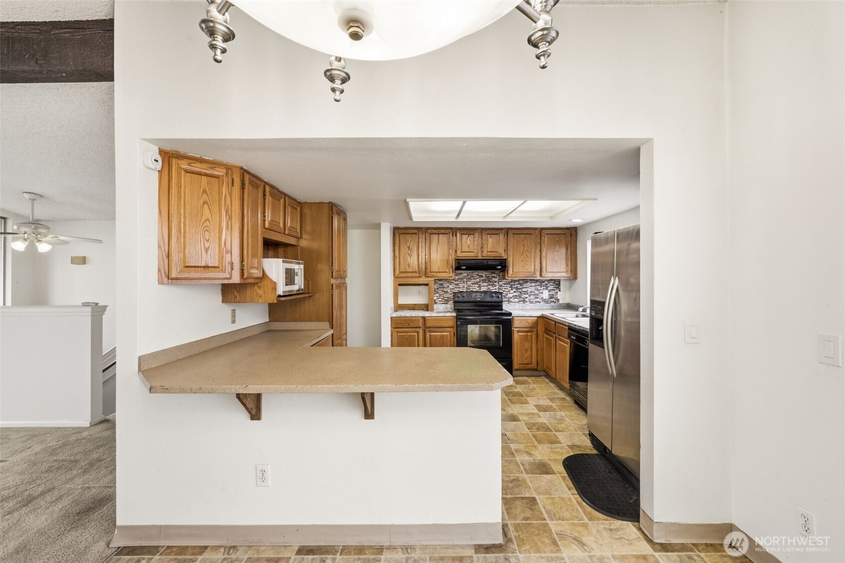 Functional kitchen with ample cabinetry, stainless steel refrigerator, and convenient breakfast bar opening to the dining area.