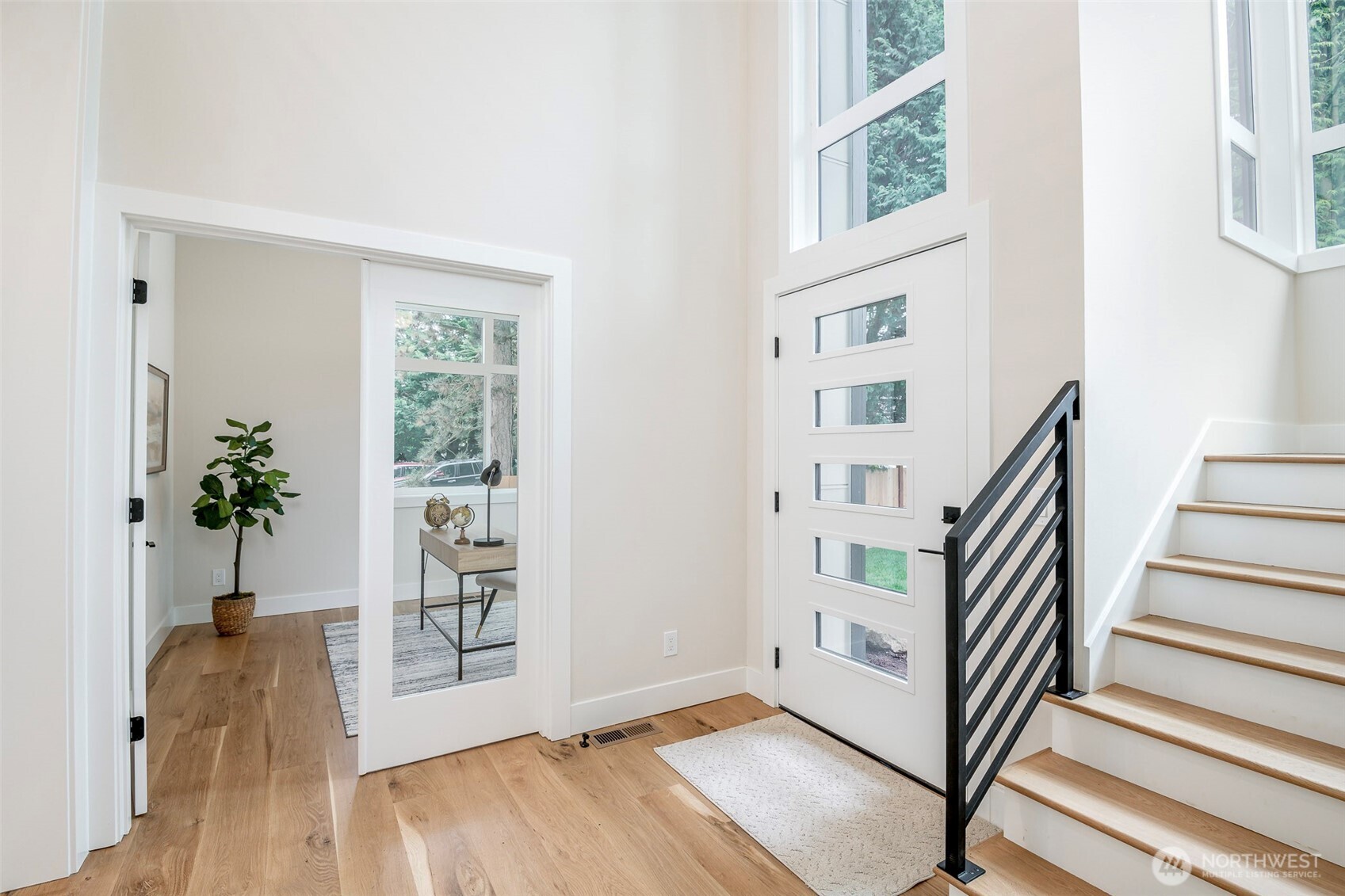 Inviting entry with soaring ceilings, wide plank hardwoods, a modern staircase, and a private office framed by glass doors for a perfect blend of style and function.