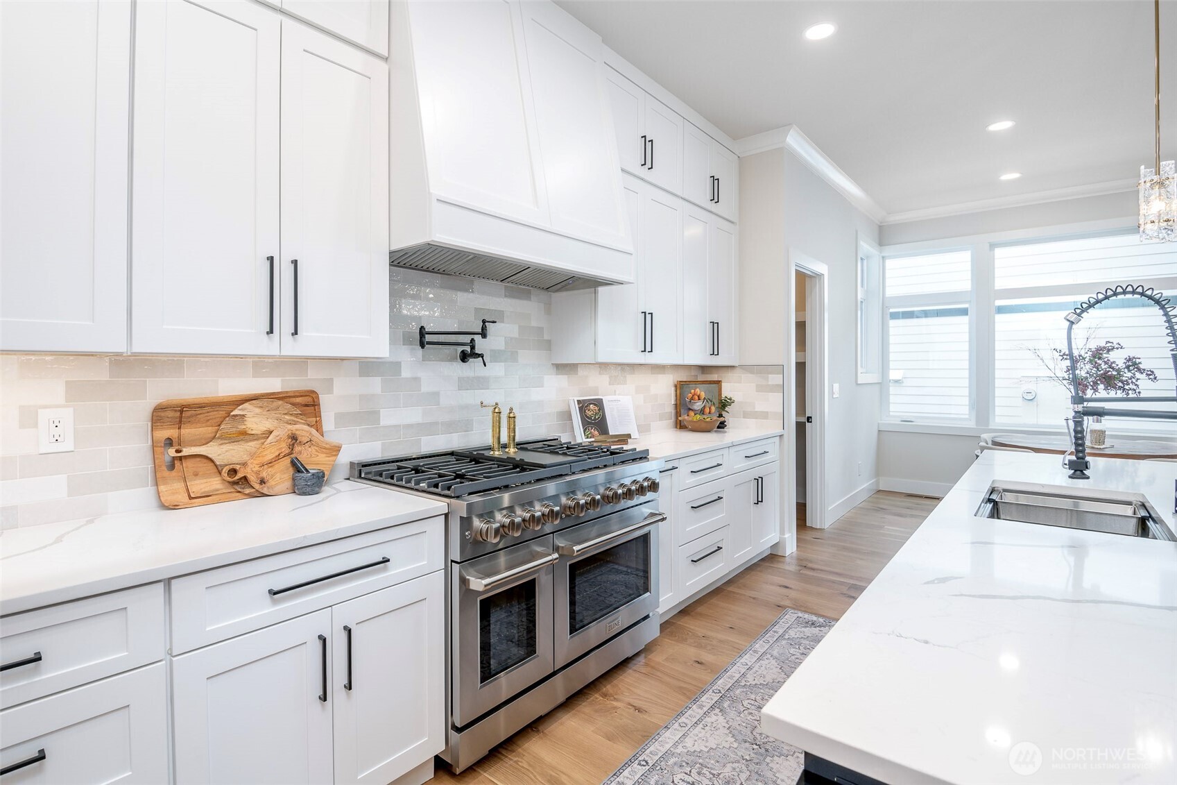 Bright and airy great room anchored by a stunning quartz island, designer lighting, and expansive windows seamlessly connecting kitchen, nook and living spaces.