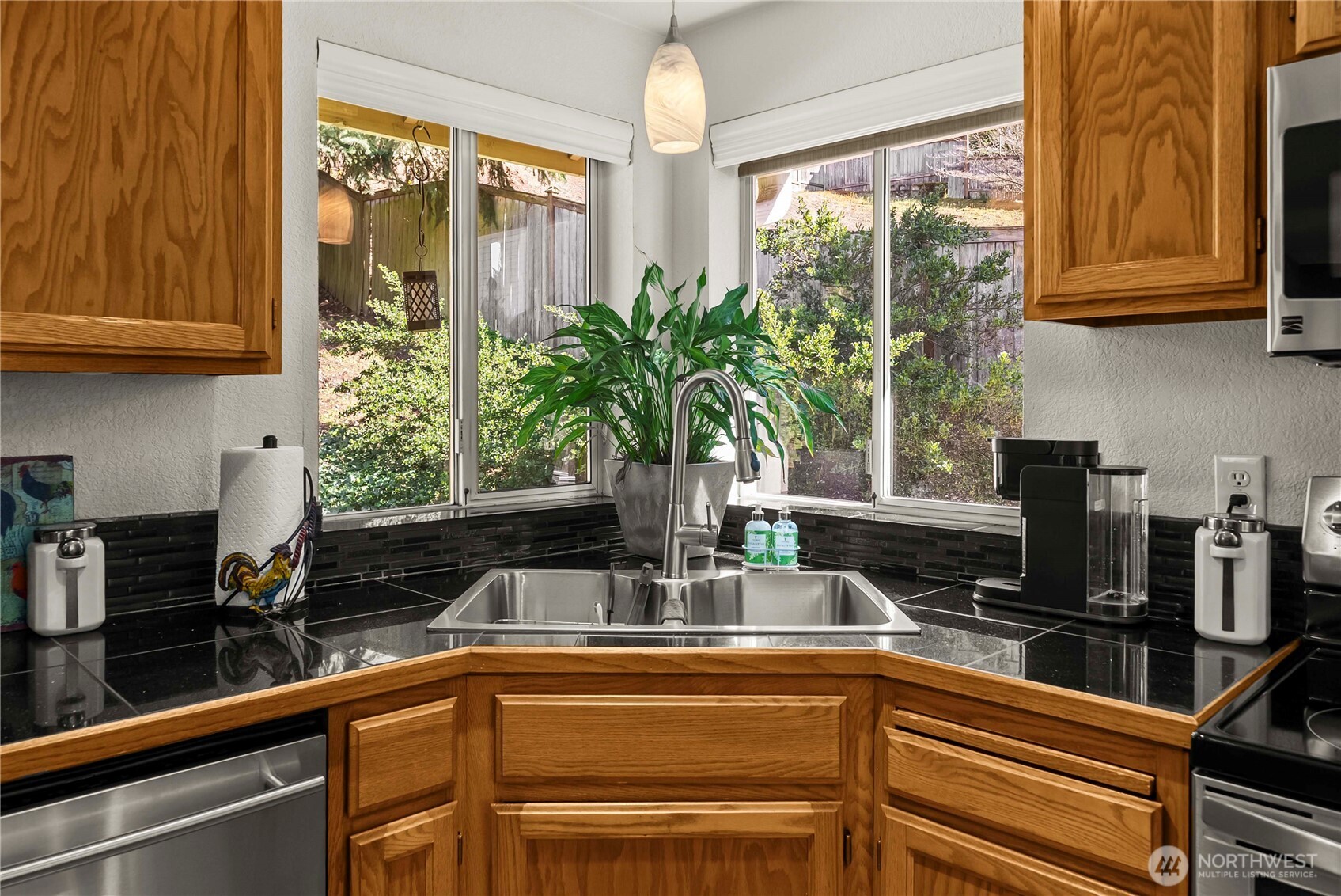 The kitchen features a corner sink with views to the backyard garden,  granite tile counters, and stainless appliances.