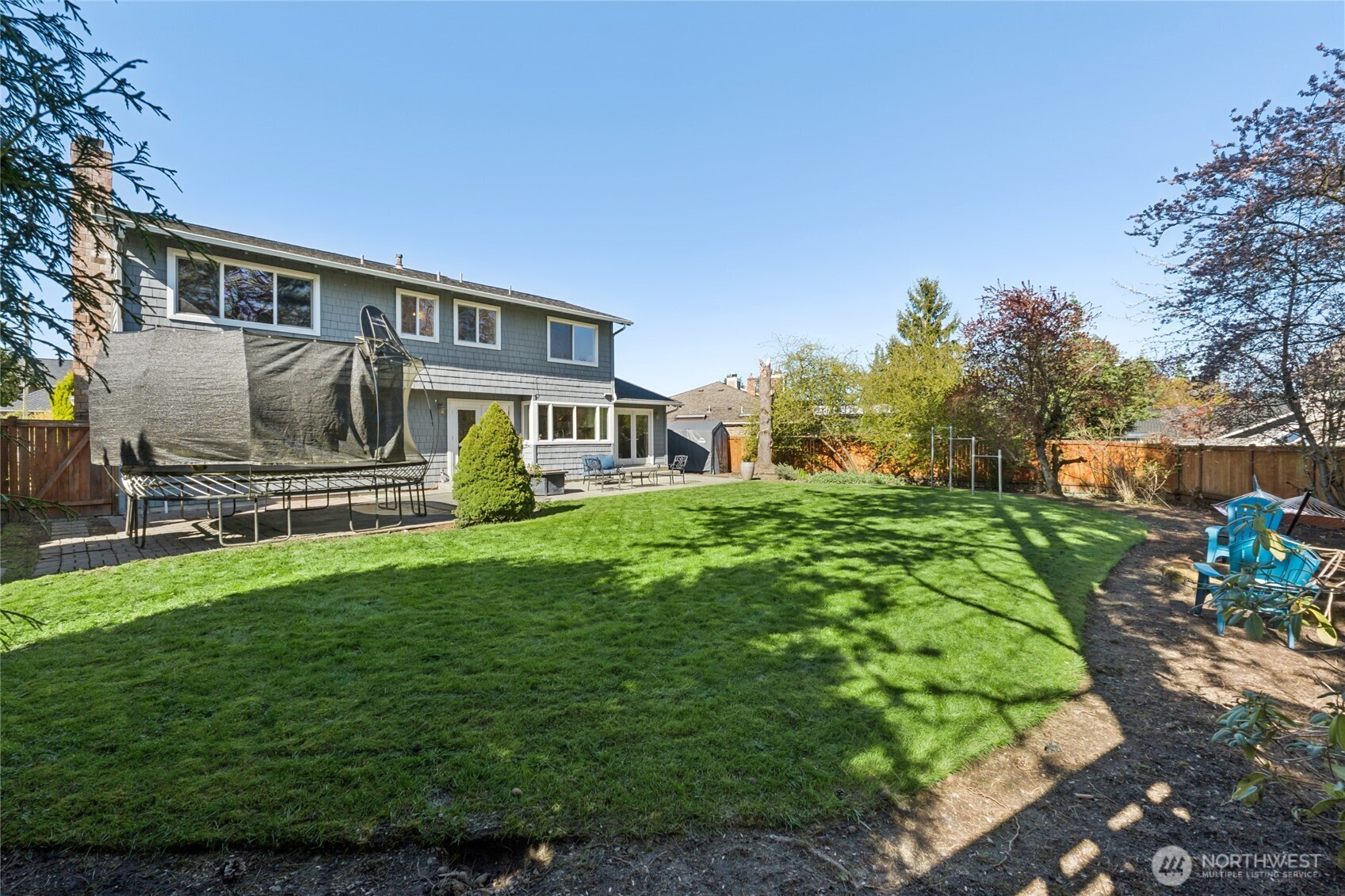 The backyard unfolds with a wide stretch of lawn, framed by mature landscaping and a full view of the home’s rear exterior.