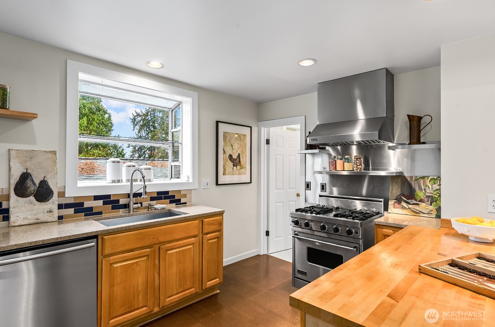 Quartz counters, tile backsplash, stainless steel appliances, wood cabinets, and a garden window above the sink.