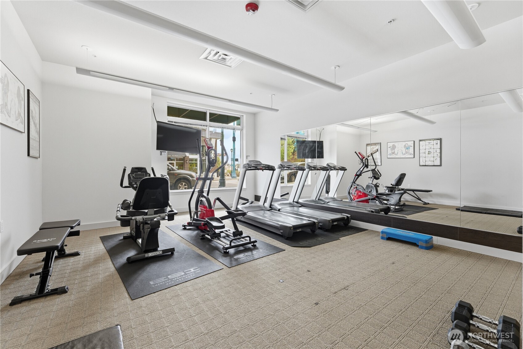 Bright community fitness room featuring treadmills, elliptical, bike, weights, and mirrored walls for versatile exercise options
