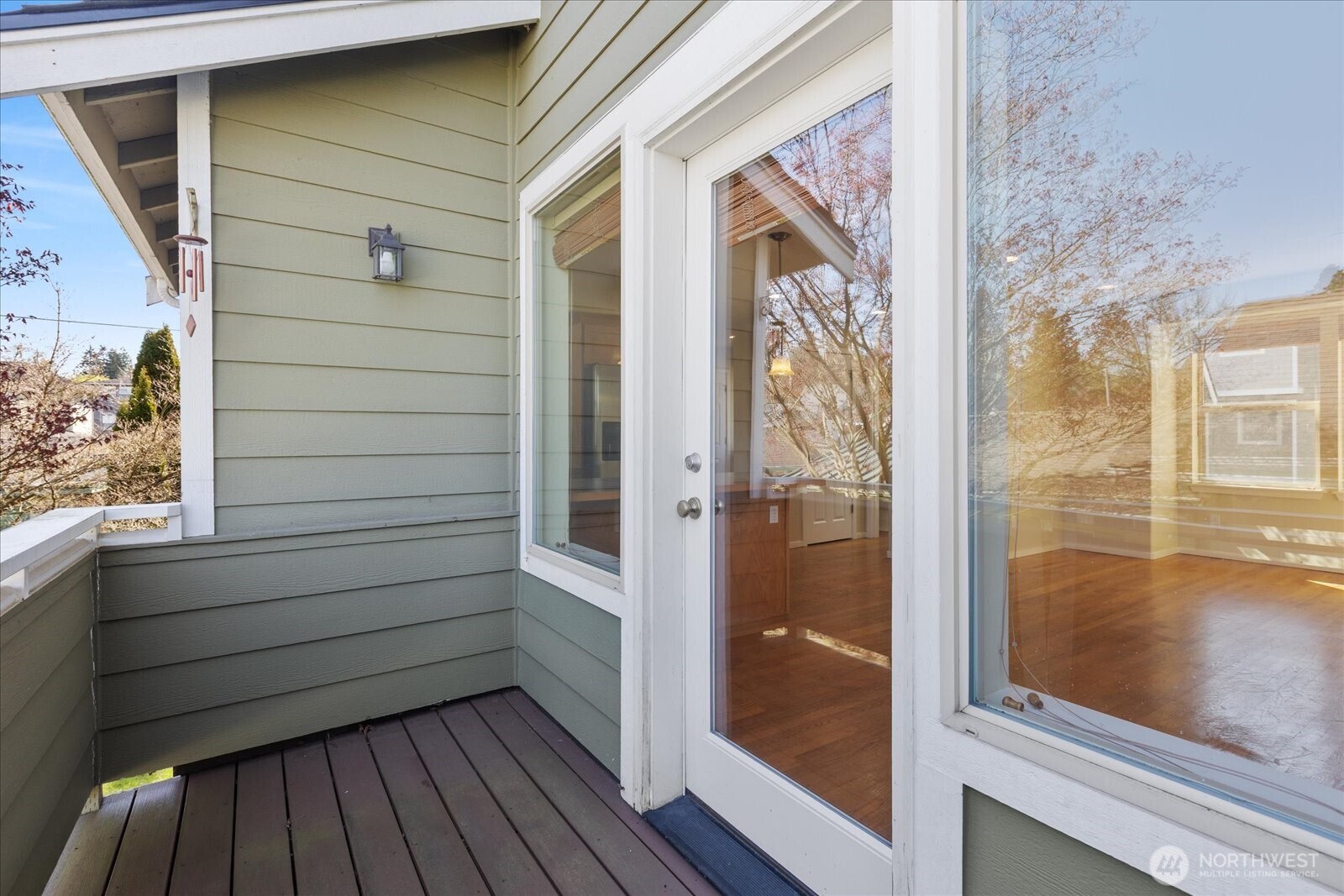 Balcony with wood decking, exterior light fixture, and access through a glass door from the interior.
