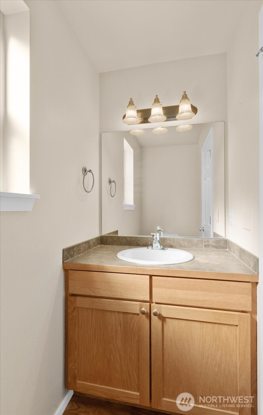 Bathroom with single-sink vanity, wood cabinetry, wall mirror, and overhead lighting.