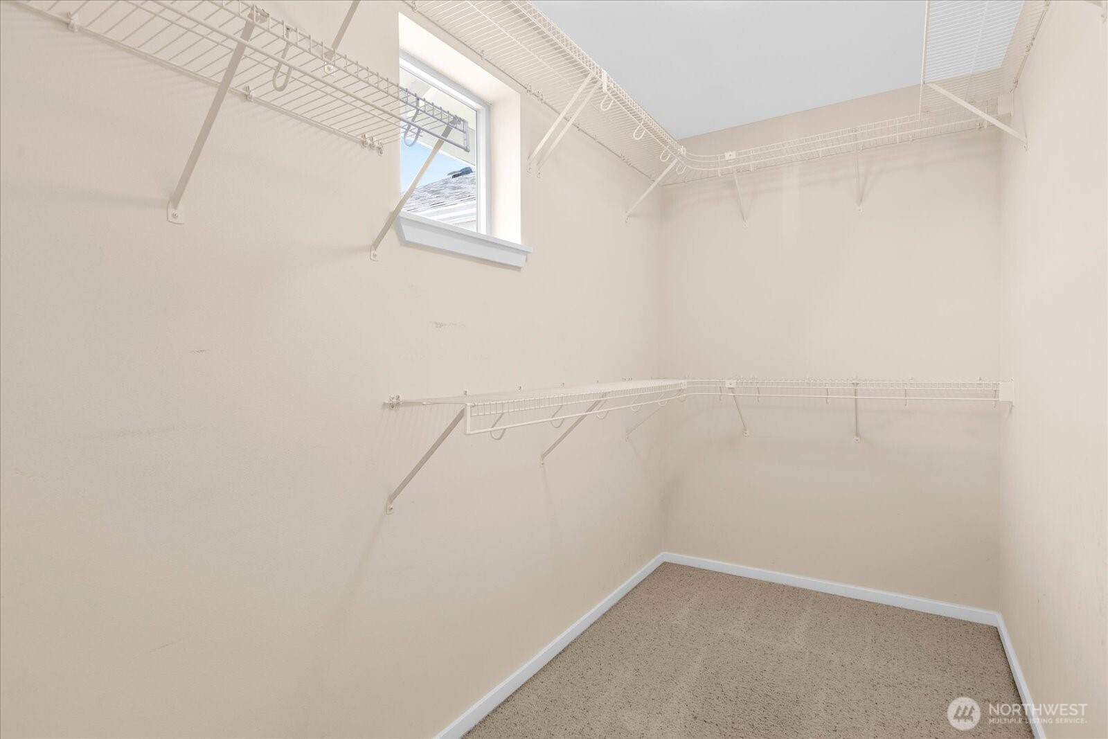 Primary walk-in closet with carpeted flooring, wire shelving, and a small window.