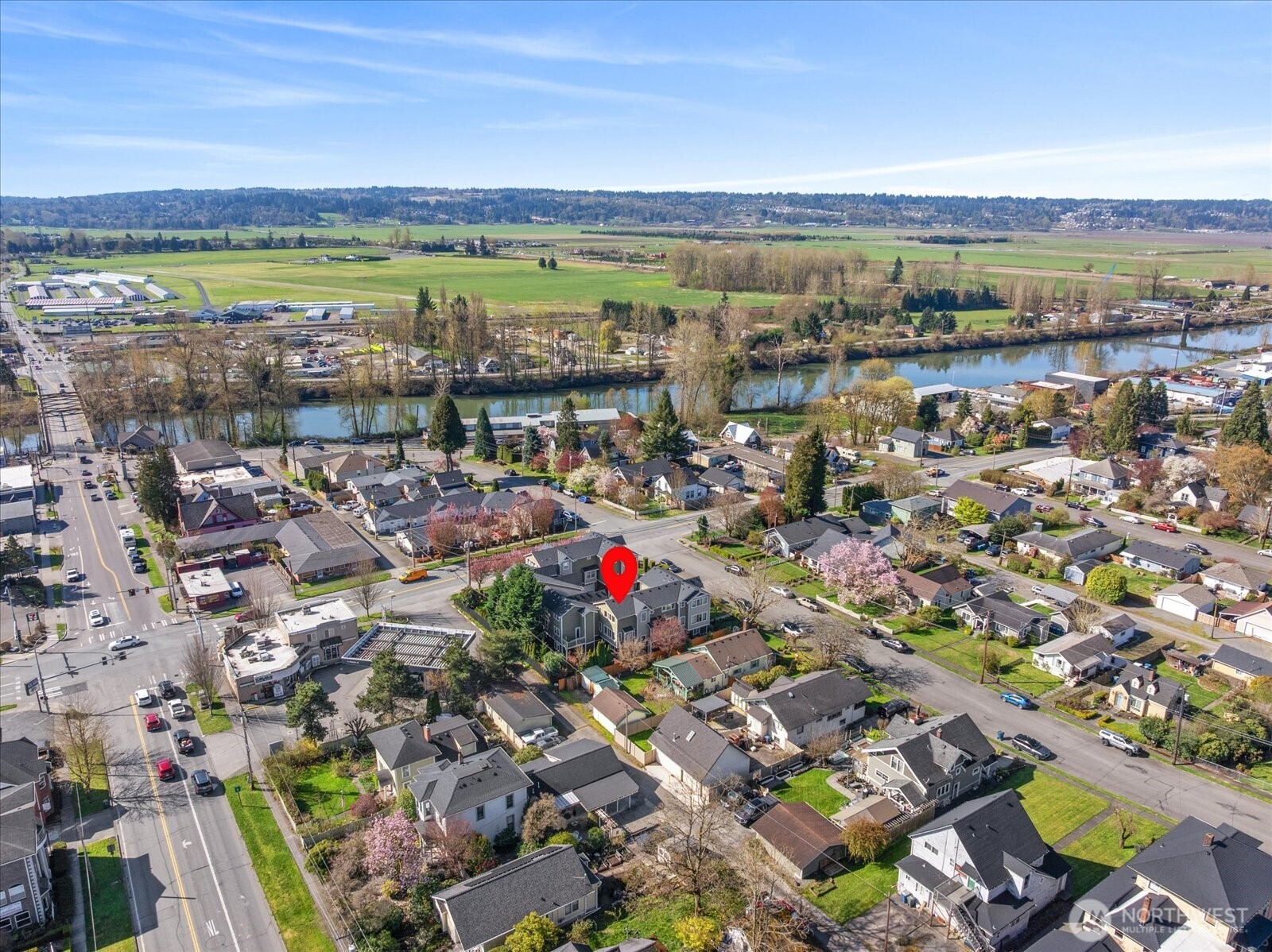 Aerial view of residential neighborhood with property marker, nearby river, and surrounding farmland.
