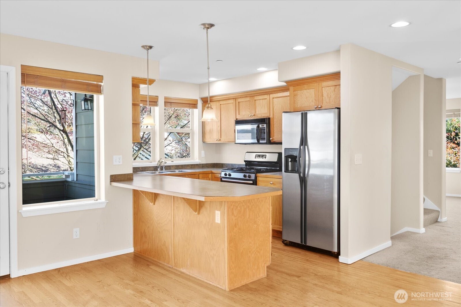 Kitchen with wood cabinetry, stainless steel appliances, center island, pendant lighting, and adjacent dining space.