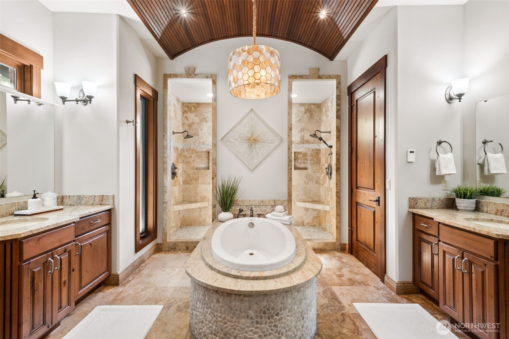 The spa-inspired primary ensuite is nothing short of stunning—featuring a dramatic barrel-vaulted wood ceiling, dual vanities with ample storage, and a striking centerpiece soaking tub. Twin walk-in showers meet in the middle with tile surrounds and create a true retreat, blending symmetry, luxury, and thoughtful design.  (Private water closet to the right)