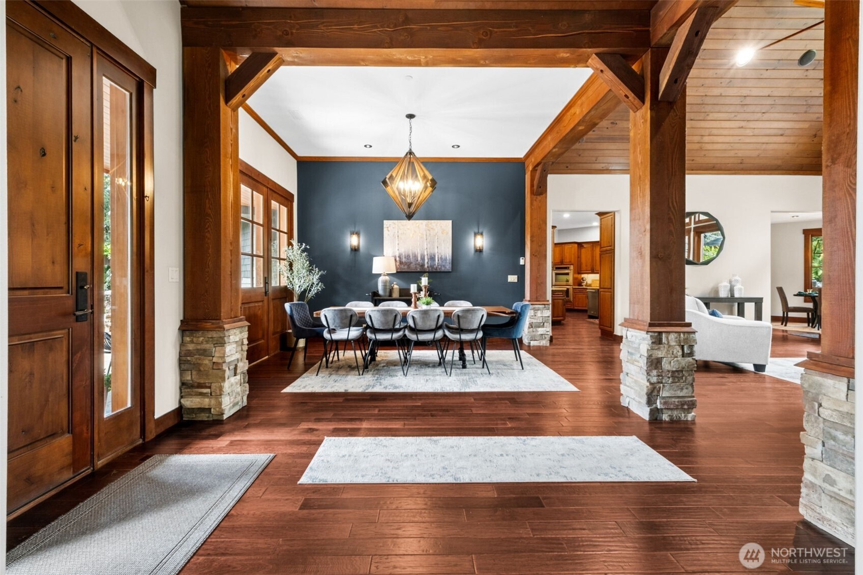 Framed by substantial timber posts with stone bases, the formal dining space makes a striking impression—anchored by a statement light fixture and rich accent wall, with clean sightlines that enhance the home’s open yet defined design.