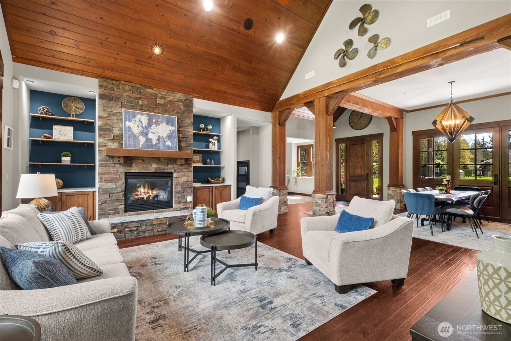 From this perspective, the open-concept layout truly shines—soaring wood ceilings, exposed beams, and a floor-to-ceiling stone fireplace with built-in shelving create a stunning focal point, while the natural flow into the dining area enhances both everyday living and entertaining.