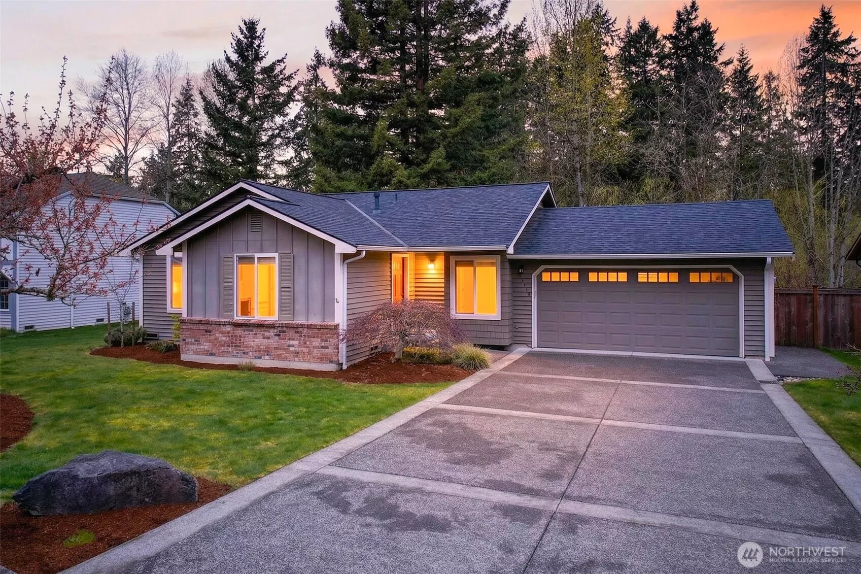 Warm evening light spills through the windows of this charming English Hill rambler, framed by mature evergreens and a lush, level front lawn that sets the stage for easy Eastside living. The wide concrete driveway and oversized two-car garage offer the storage and convenience that buyers in Redmond genuinely appreciate.