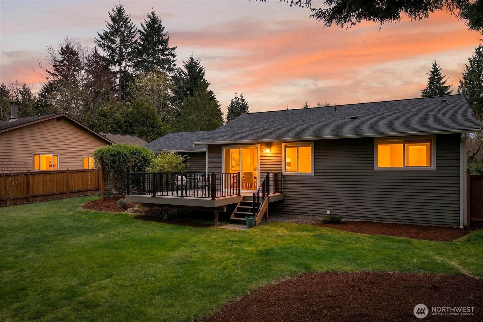 At dusk, warm light glowing through the rear windows and sliding glass doors transforms this backyard into an inviting evening retreat. The 2020 deck, lush lawn, and surrounding evergreen canopy come together in a scene that perfectly captures the appeal of Pacific Northwest outdoor living.