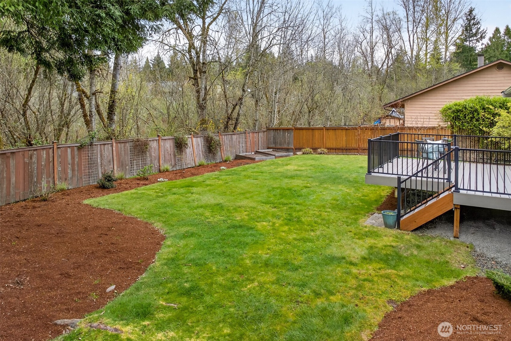 The rear yard backs directly to a lush greenbelt with native trees and natural growth that provides a year-round privacy buffer you simply can't manufacture. The level lawn, freshly mulched planting beds, and deck access steps make this a yard that's both beautiful and genuinely usable from day one.