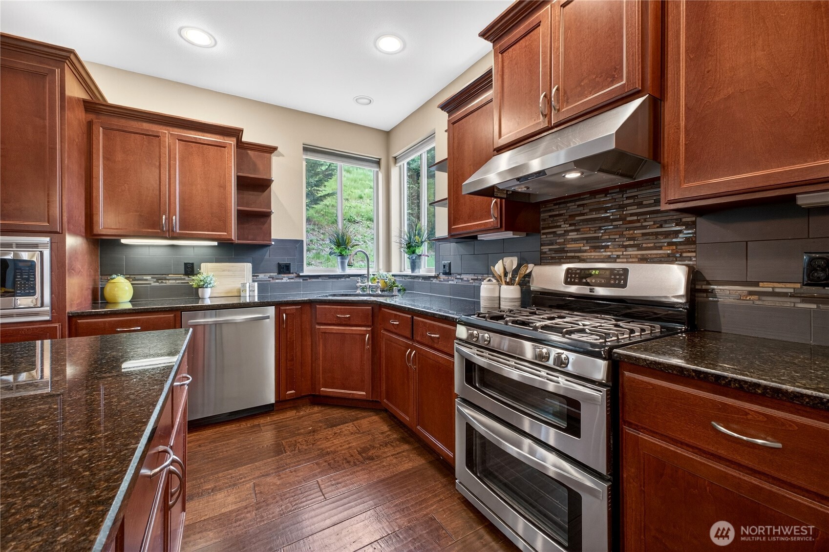 Additional view of the kitchen showcasing the upgraded double oven with gas range, and a sink perfectly positioned beneath dual windows overlooking the backyard.