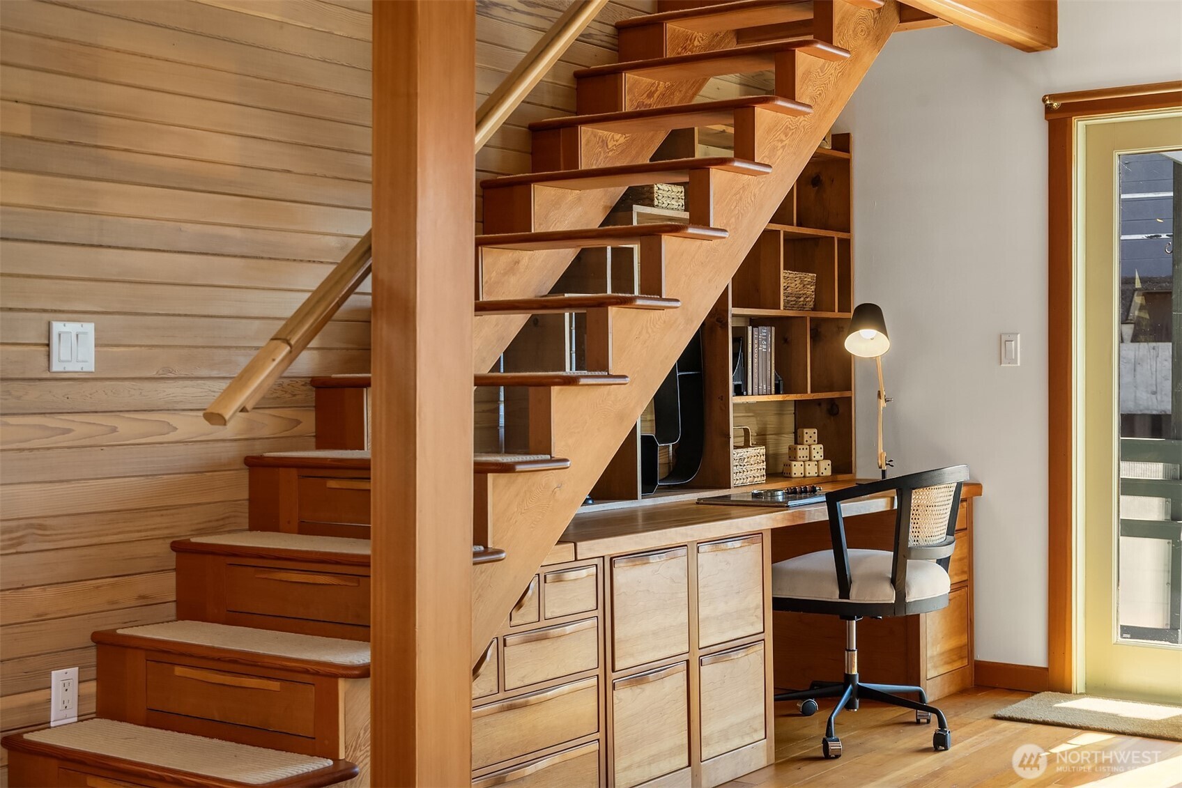 One of the home's most inventive features: a fully custom built-in desk and shelving system beneath the staircase, crafted in warm wood. The staircase wtih hidden drawers, storage for all your odds & ends.