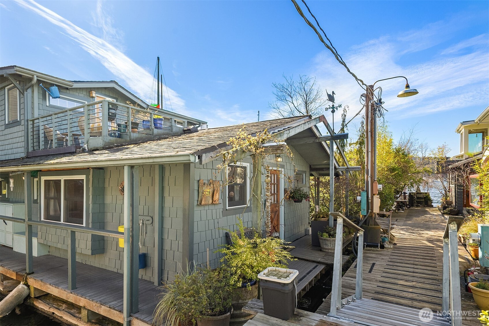 The home from the dock side, with the rooftop deck visible above and the water lapping gently below — a complete picture of floating home life.