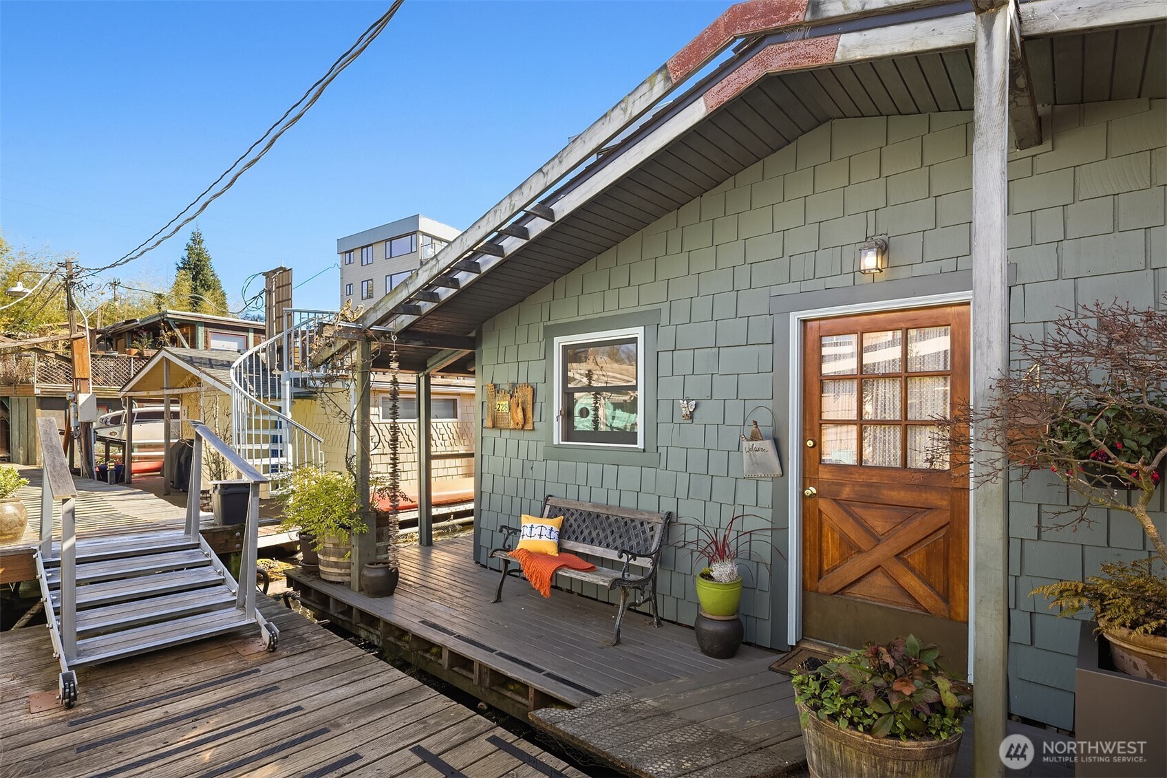 The sage green shingle exterior and warm wood Dutch-door give the home an instantly welcoming face, with a bench and potted plants making the entry dock feel like a front porch.