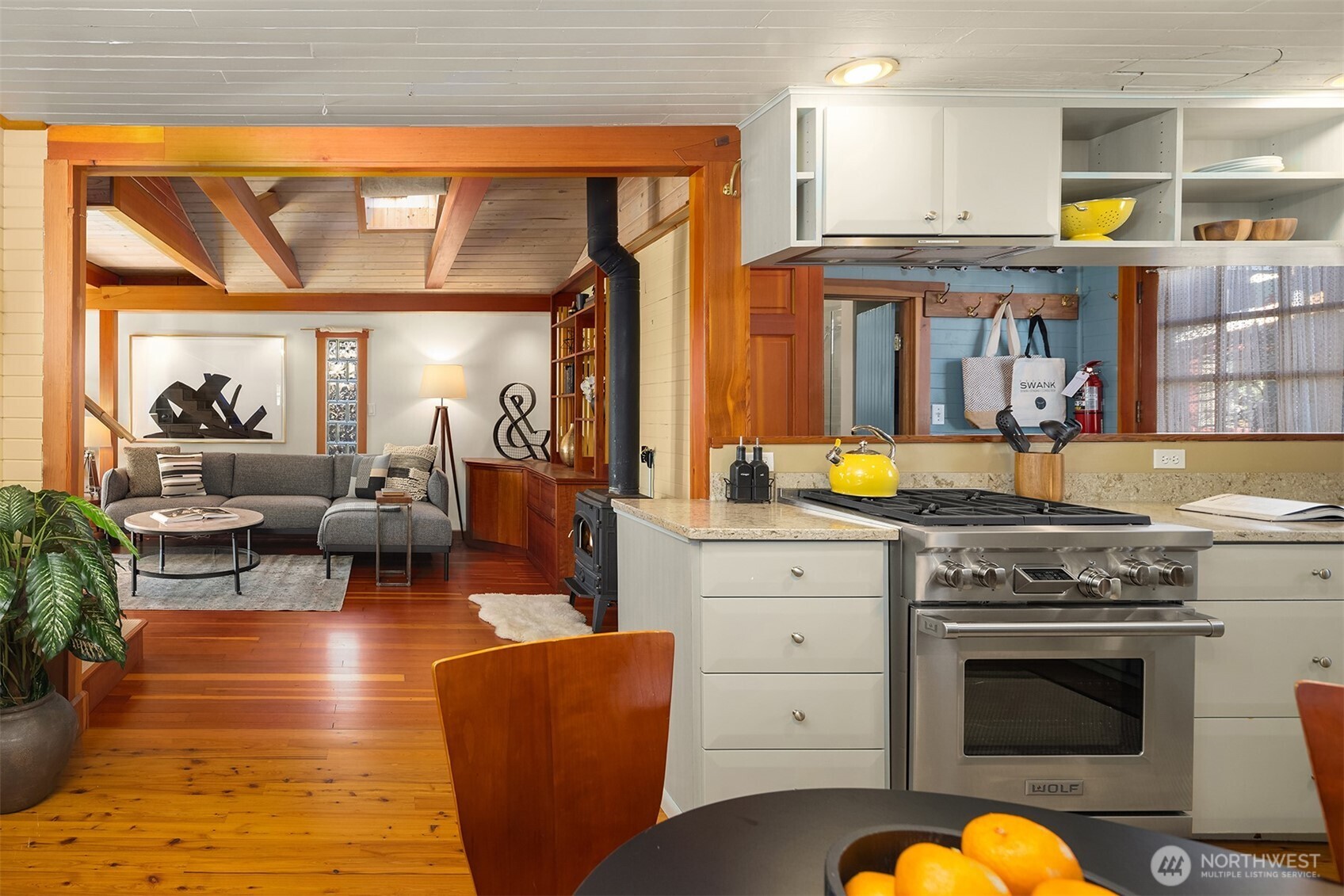 From the kitchen, the professional range takes center stage while the eye travels through to the living room's beamed ceiling and glimpses of the cast-iron wood stove.