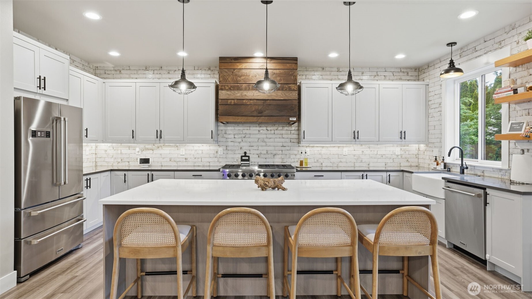 True entertainer’s kitchen with oversized island, custom hood, open shelving, quartz countertops, commercial appliances, walk-in pantry, and wine fridge.