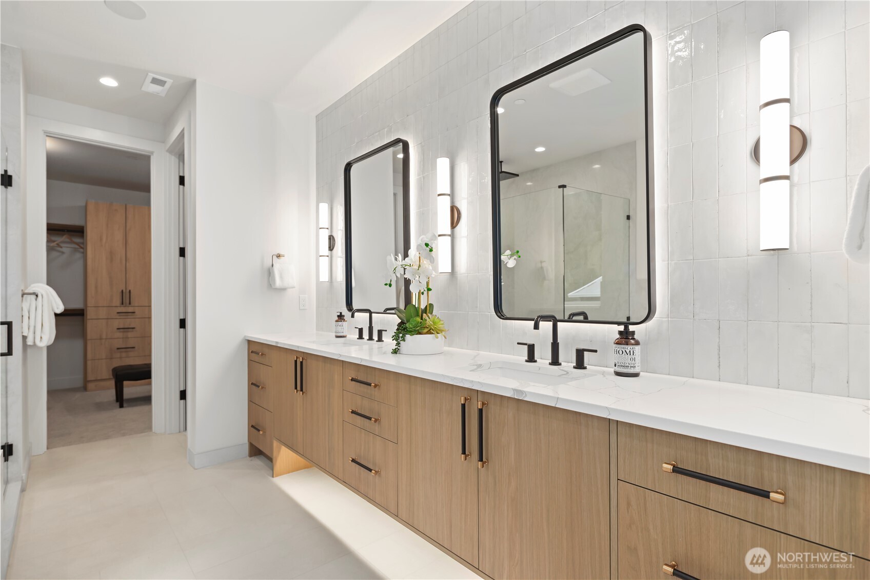 Dual vanity with LED backlit mirrors, warm wood cabinetry, slab quartz counters, and designer hardware. Prewired for ceiling speakers plus motion-activated toe-kick lighting.