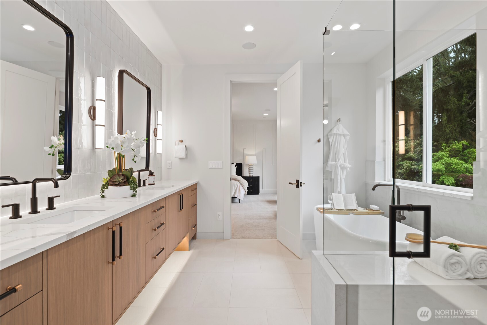 Clean-lines double vanity paired with matte black fixtures, framed backlit mirrors, wall sconces, and floor-to-ceiling satement tile backsplash wall.