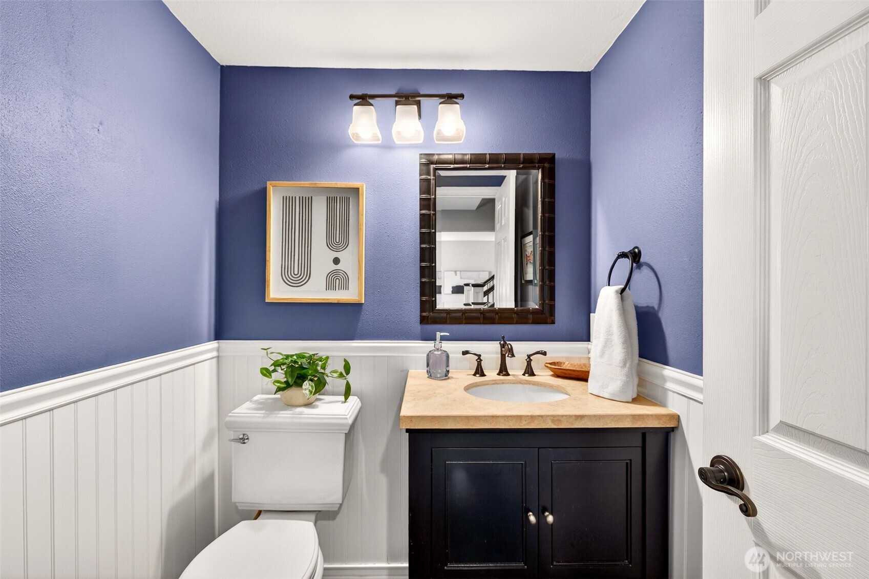 The main-level powder room makes a bold, stylish statement with rich blue walls, board-and-batten wainscoting, a dark-finish vanity, and warm lighting — a thoughtfully designed space that leaves a lasting impression on guests.