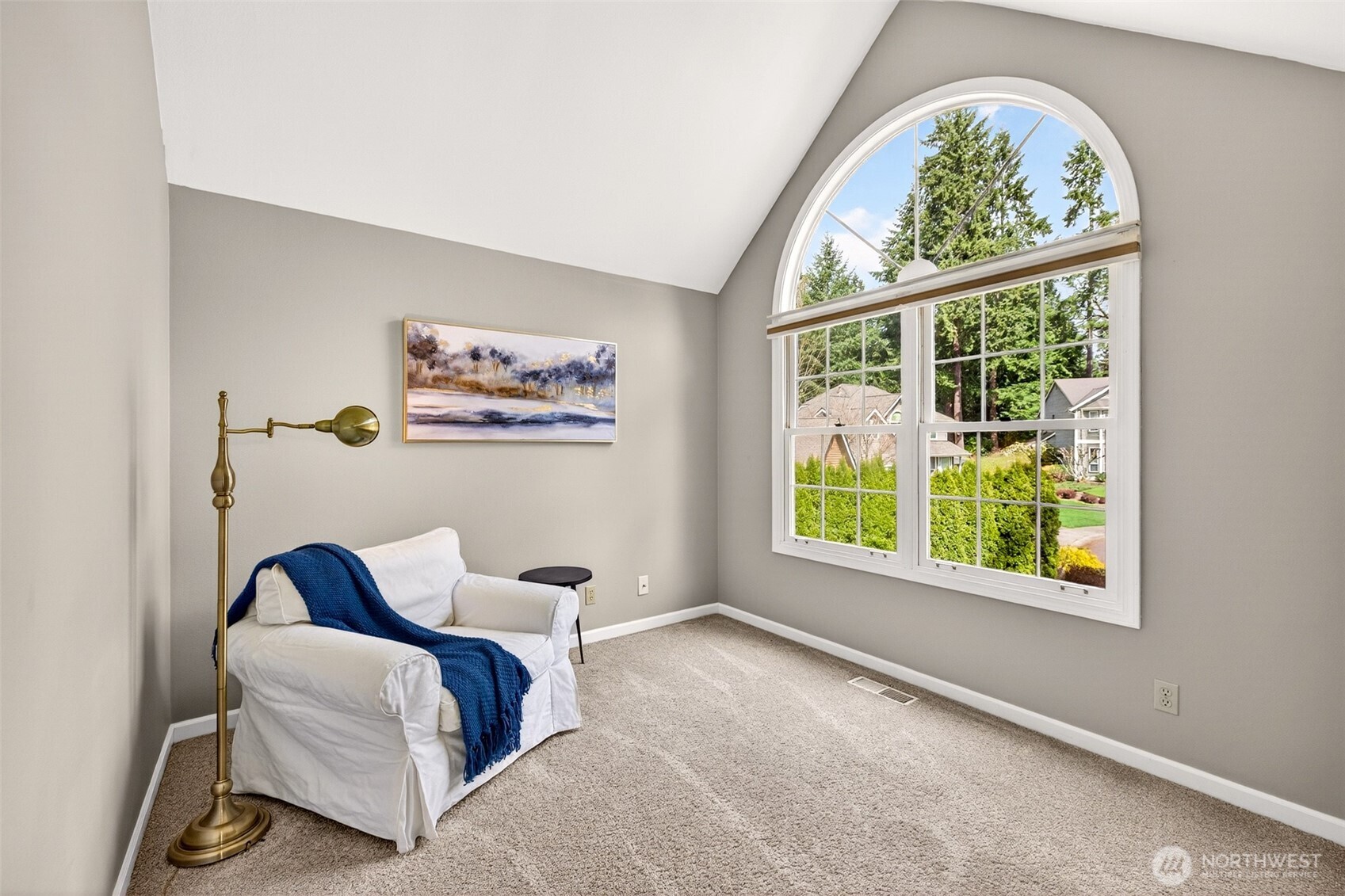 The primary suite's vaulted sitting area features a dramatic arched window framing a lush evergreen outlook — a serene, light-drenched space perfect for a morning reading nook or a quiet end-of-day escape.