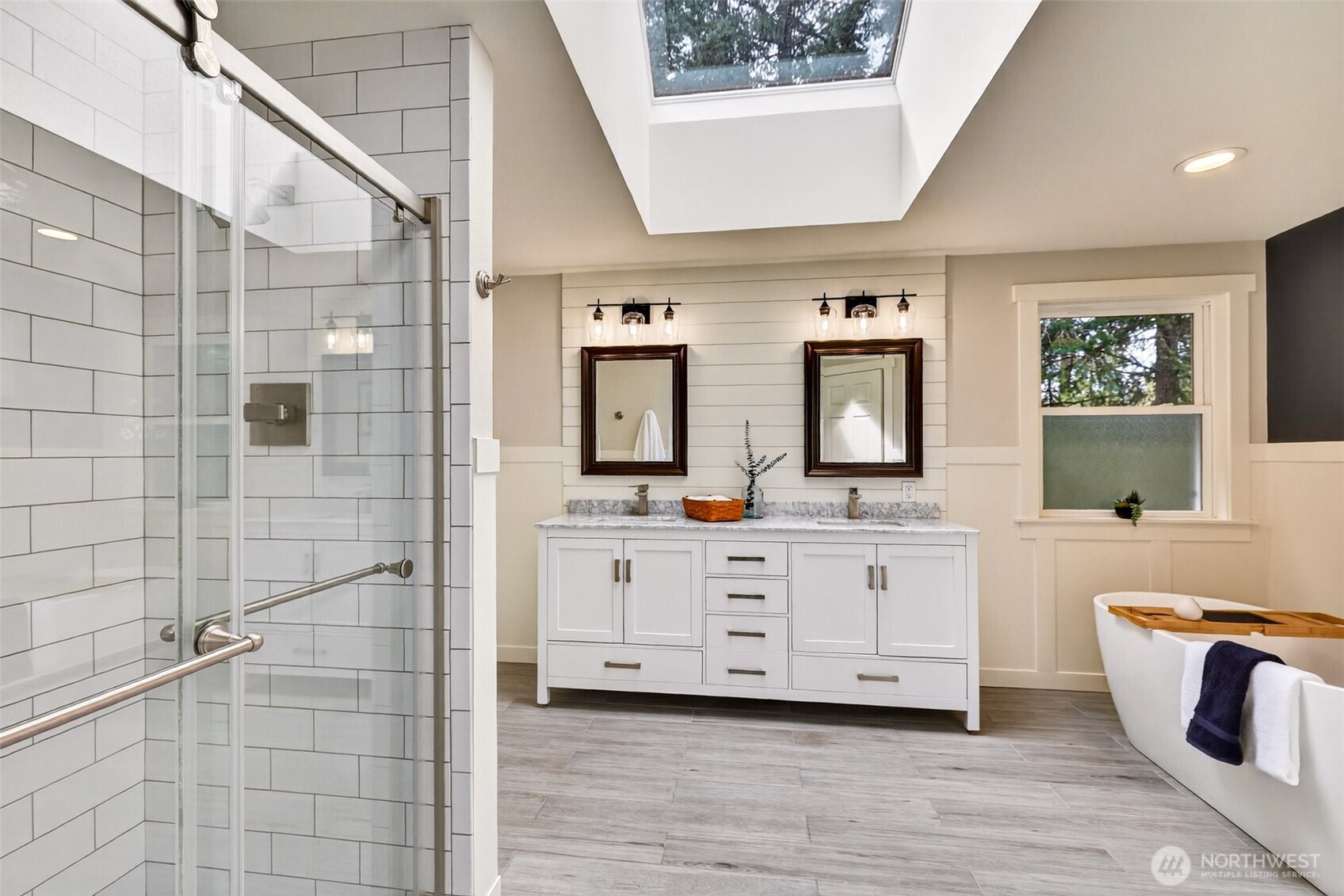The updated primary bath is a true spa retreat — featuring a skylight that bathes the space in natural light, dual-sink vanity with marble countertops, shiplap accent wall, freestanding soaking tub, heated floors, and a walk-in tile shower.
