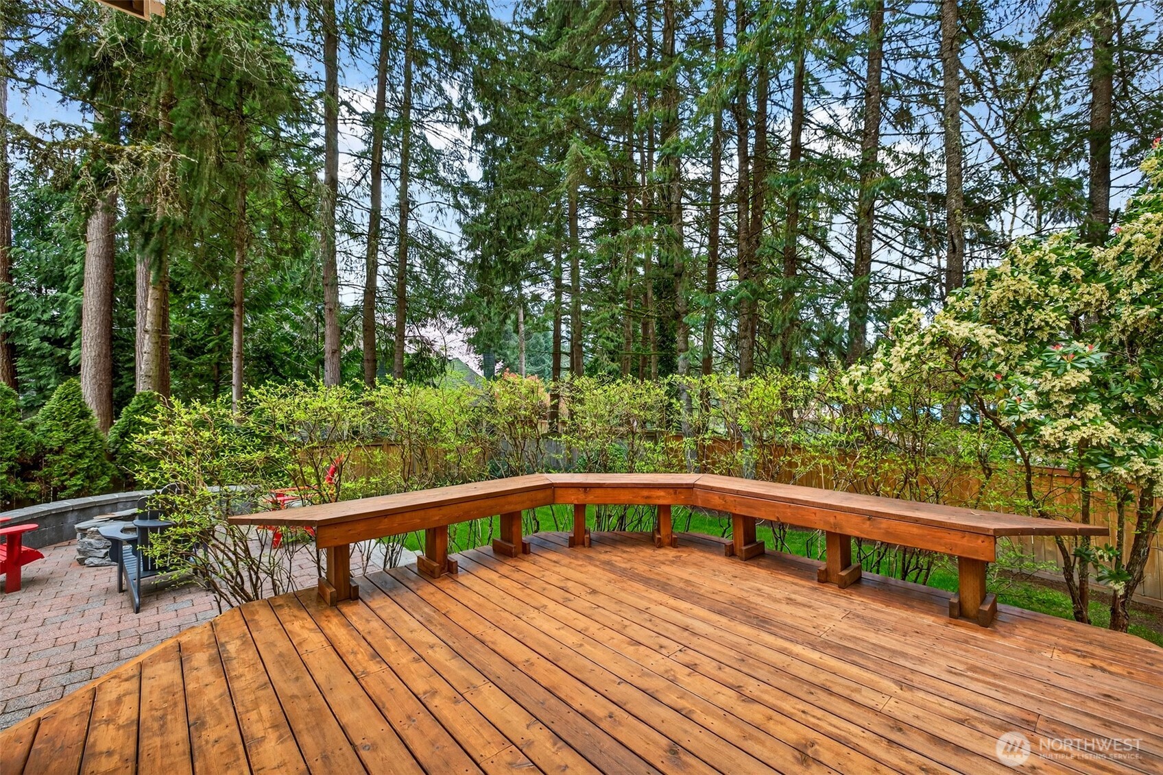 The expansive lower deck level features a custom built-in bench wrapping the perimeter — a generous, versatile outdoor space designed for effortless entertaining, summer gatherings, or simply enjoying the serene wooded backdrop.