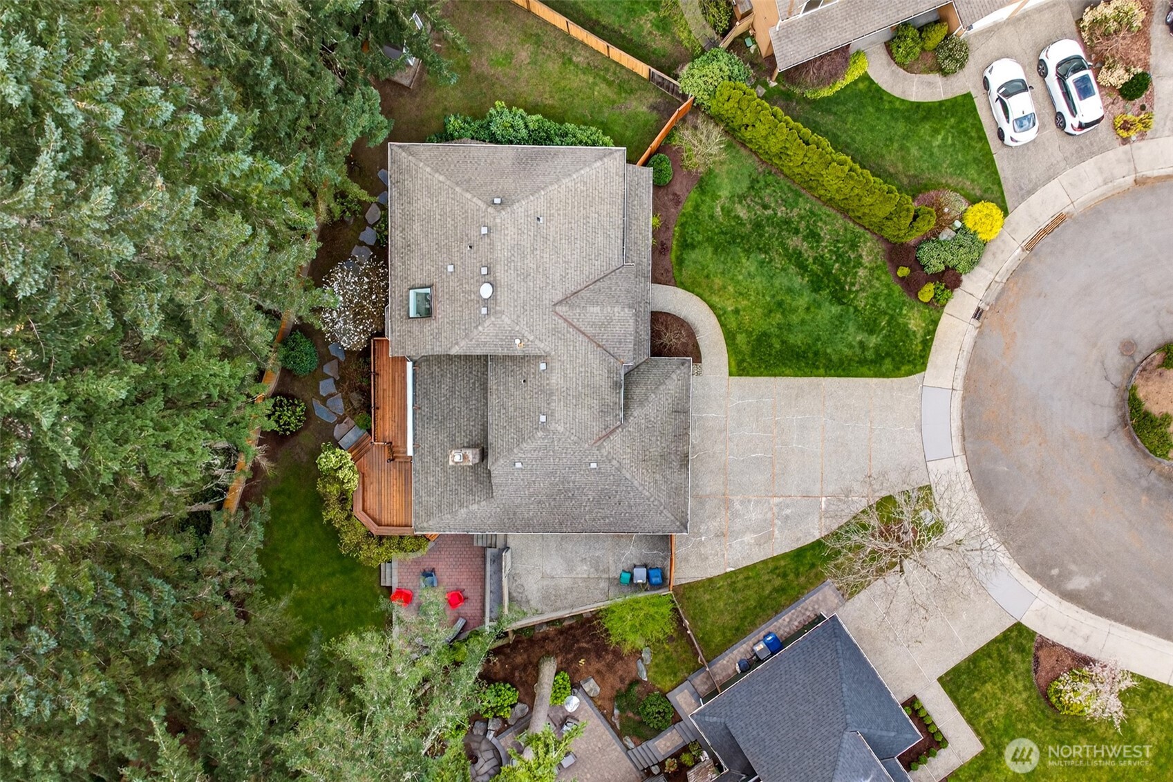 An aerial overview reveals the exceptional lot layout — showcasing the wide concrete driveway, lush front lawn, multi-level rear deck, patio, and the privacy-enhancing tree canopy that defines this English Hill setting.